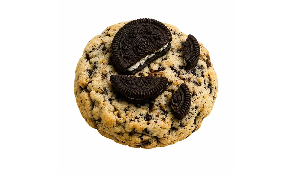 Cookies and cream cookie topped with broken mini Oreo cookie pieces on plain white background at Sweet Cottage Cafe, a Dessert shop in Lexington